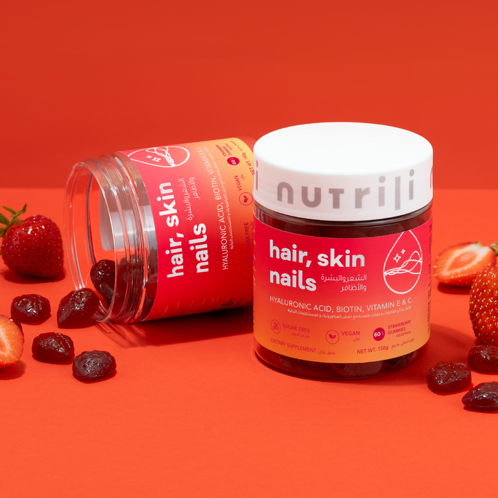Two jars of Nutrilite hair, skin, nails supplement on an orange background with strawberries and raisins.